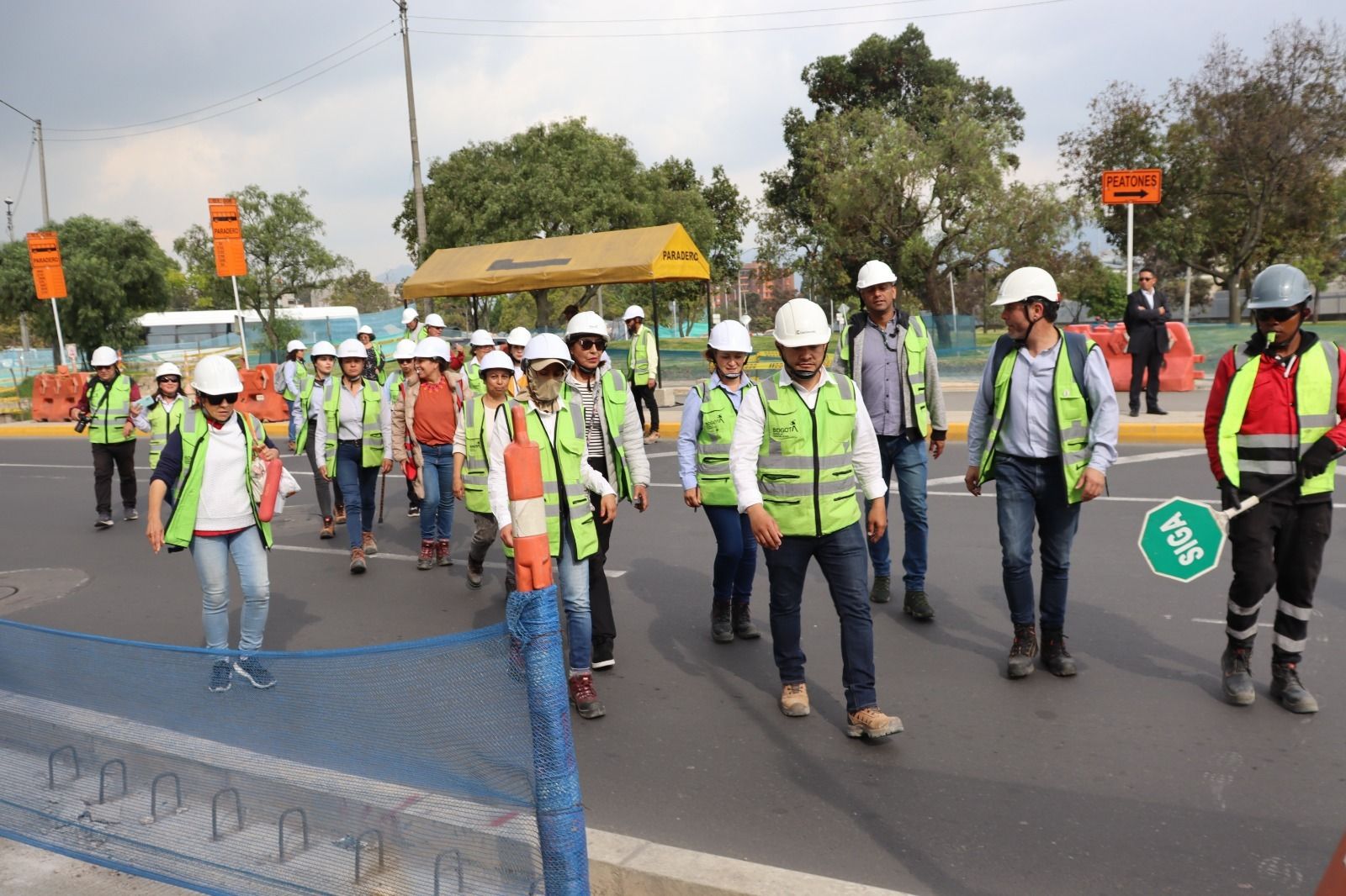 Un grupo de personas con chalecos verdes son guiados por un trabajador de obra para atravesar una de las vías en construcción