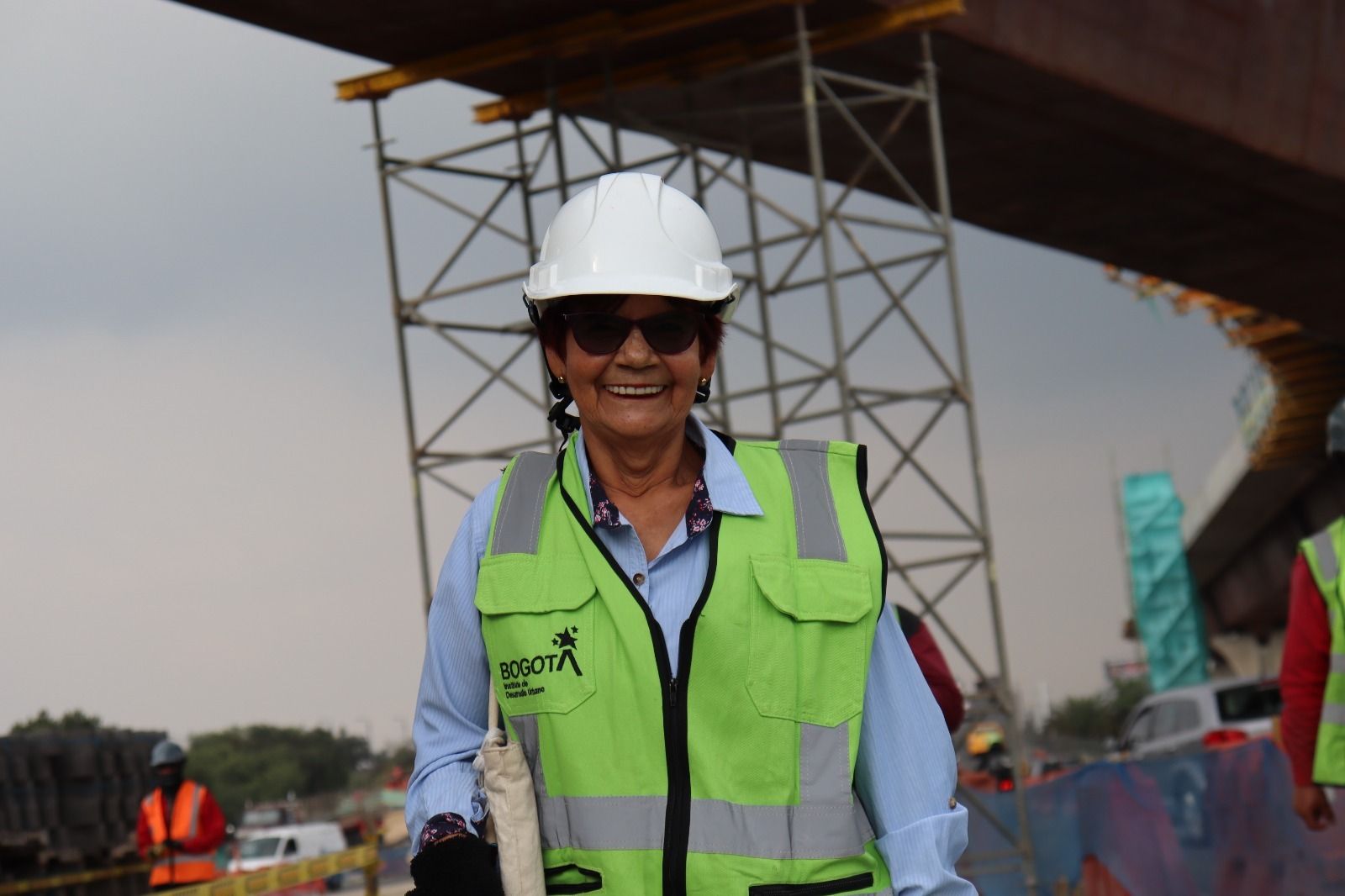 Una señora, con casco y chaleco verde, sonríe a la cámara durante la visita