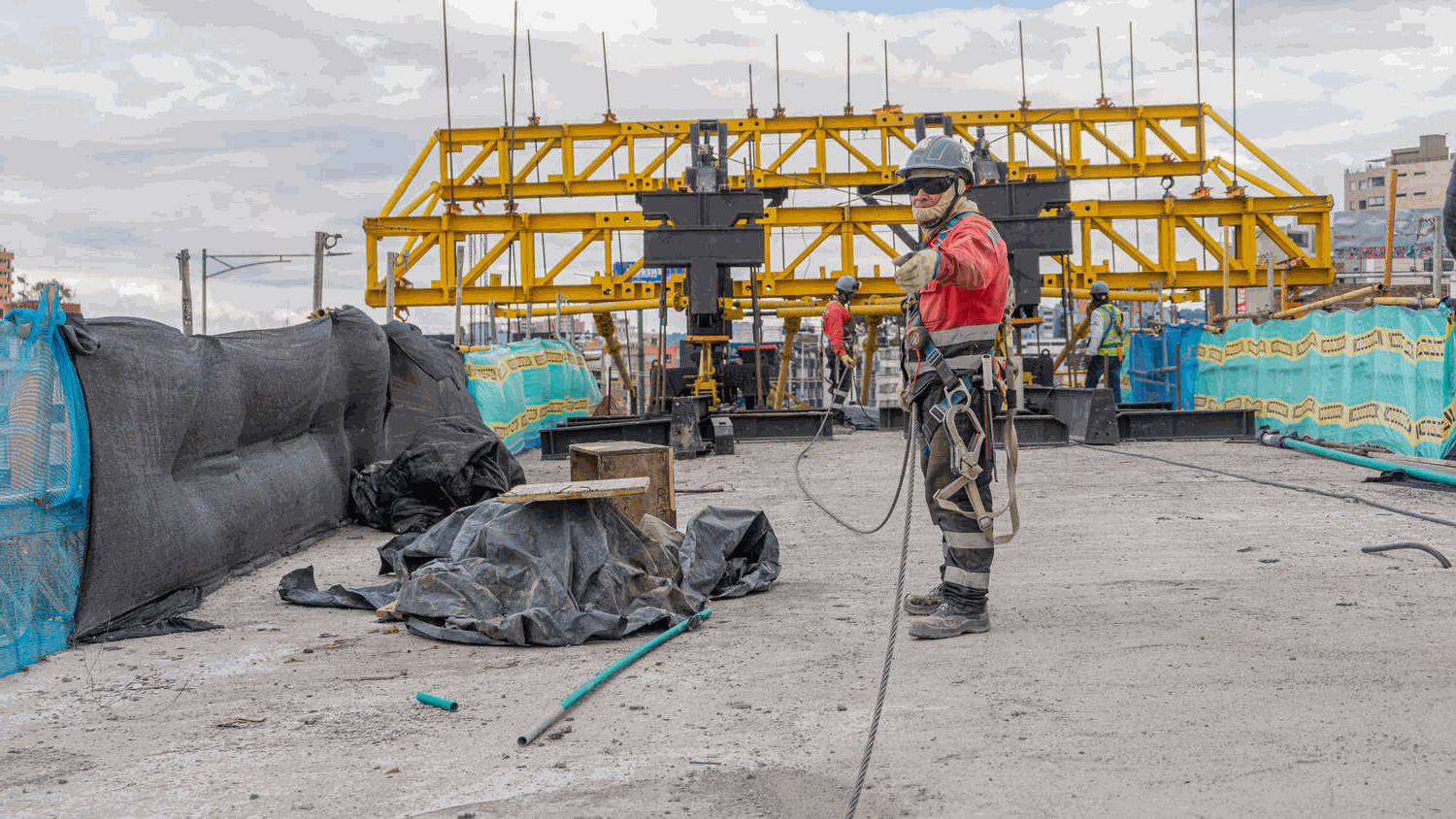 Un trabajador de obra señala la cámara para dar una indicación, mientras al fondo de se la estructura de un puente en construcción