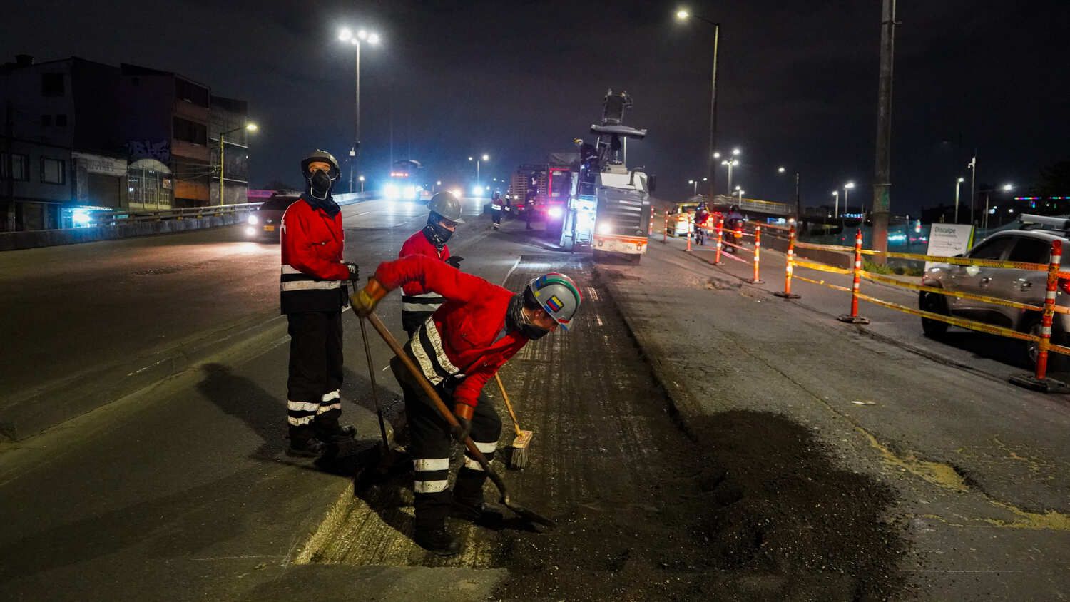 Tres trabajadores arreglan la vía de un puente particular, al fondo se ve una máquina pavimentadora
