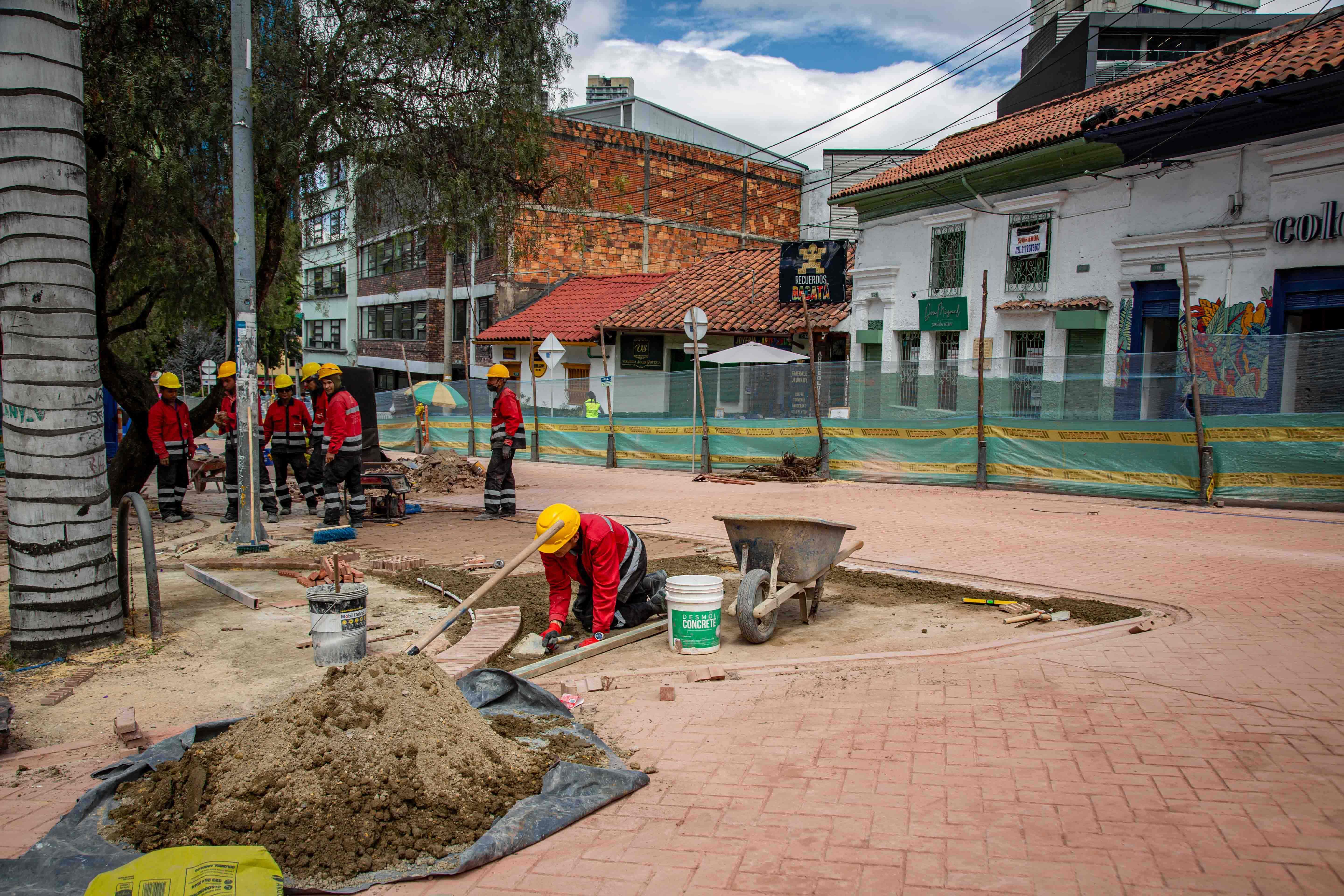 Un grupo de trabajadores de obra se reunen alfondo de la fotografía. Adelante, uno, de rodillas, arregla el adoquín en el Eje Ambiental