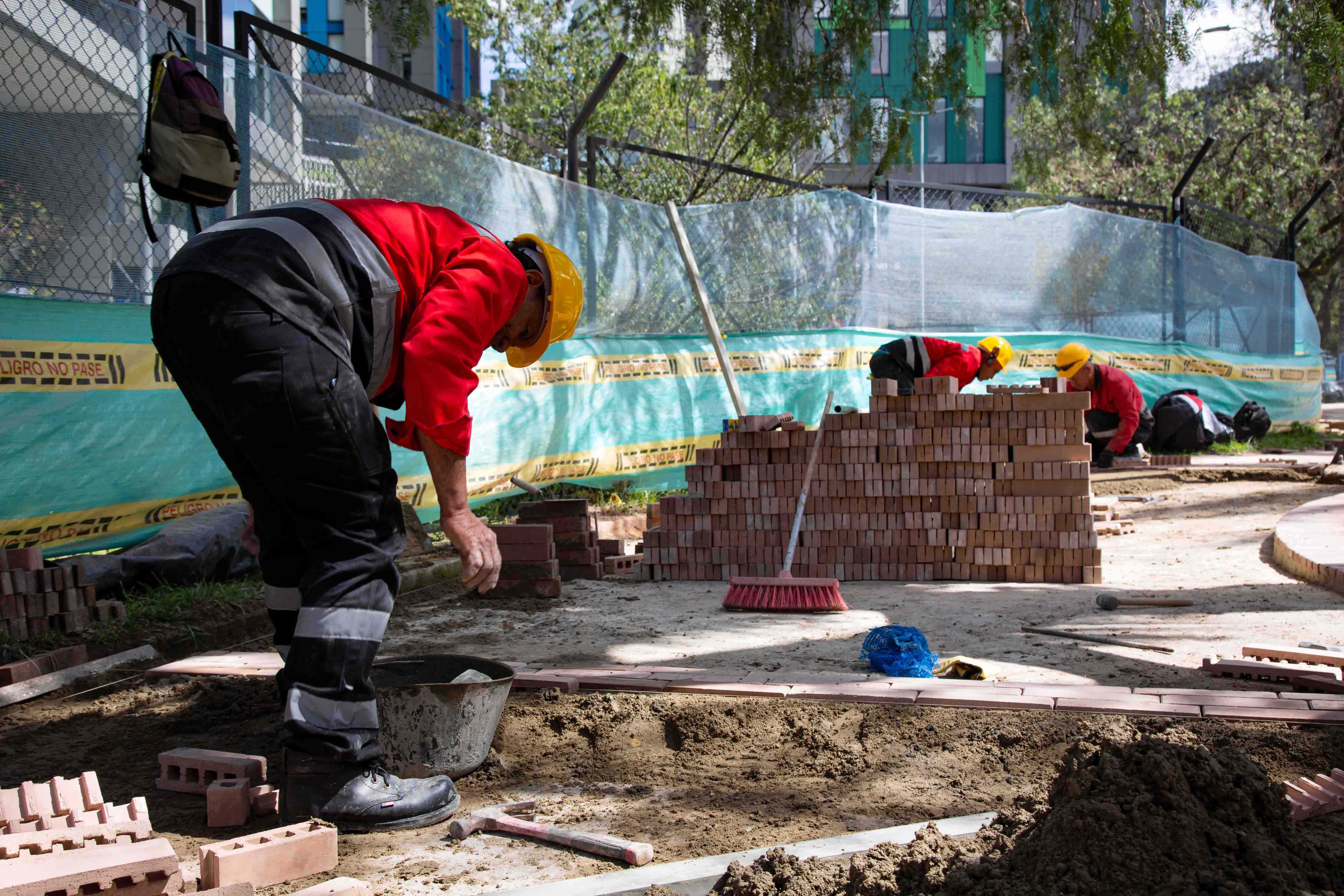 Un empleado de obra se agacha para batir la mezcla que sirve para arreglar el adoquí n en el Eje Ambiental. Al fondo otros dos pegan los ladrillos al piso