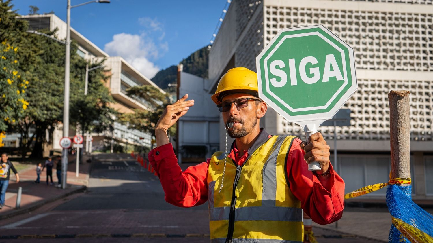 Un trabajador de obra sostiene una paleta que dice siga y hace una señal que indica que se puede continuar