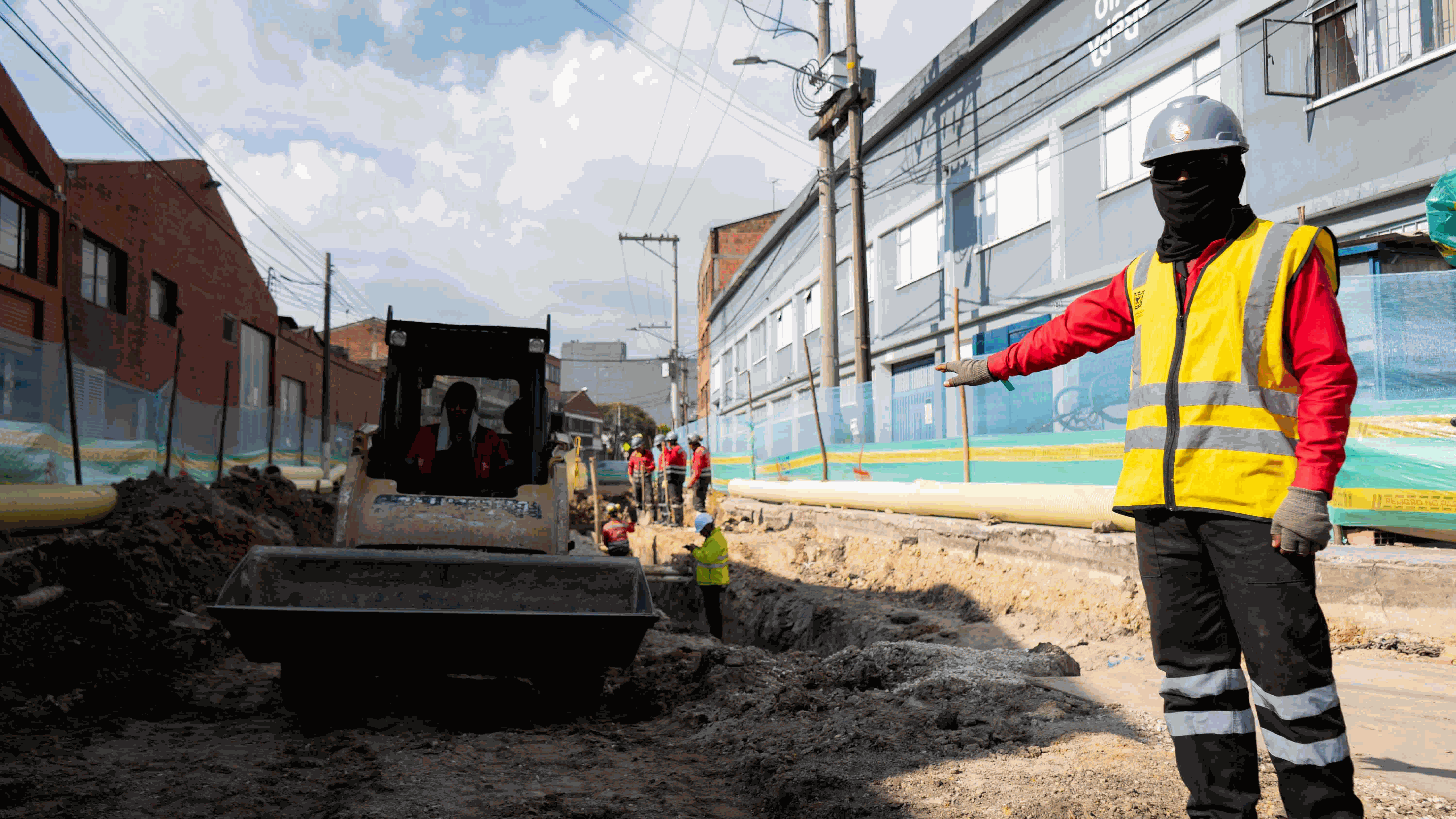 Un trabajador de obra, identificado con chaleco y casco, muestra el trabajo que realiza una máquina aplanadora en una vía que ya ha sido excavada