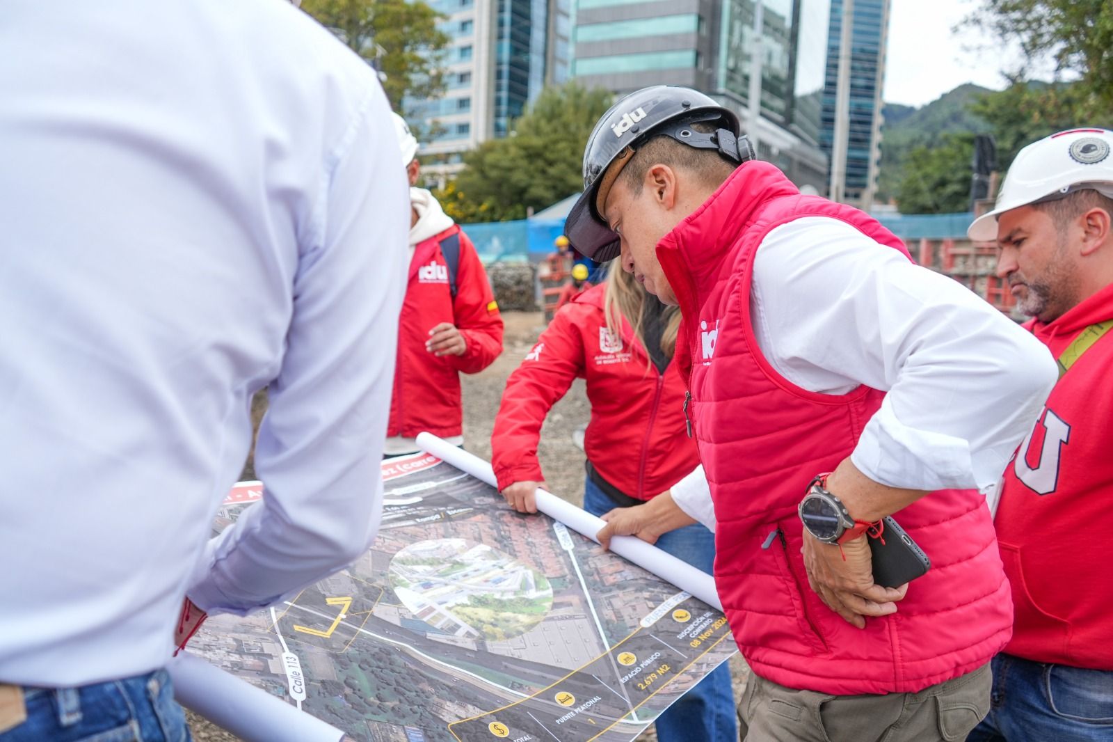 Orlando Molano, director del IDU y su equipo técnico inspeccionan sobre una mesa los planos del puente peatonal en el frente de obra.